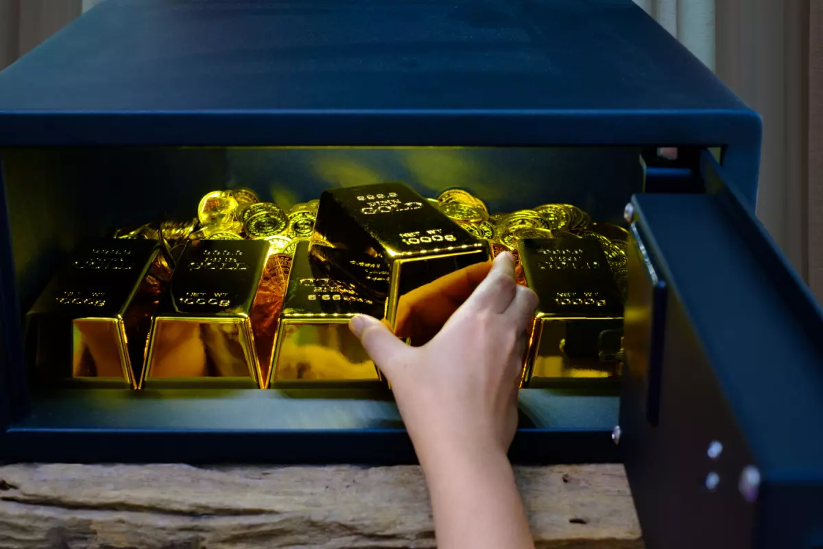 Hand placing gold bar in storage full of gold coins and bars